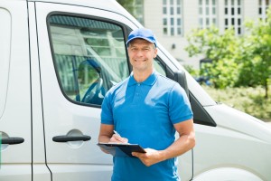Young Happy Male Worker In Front Of Truck Writing On Clipboard